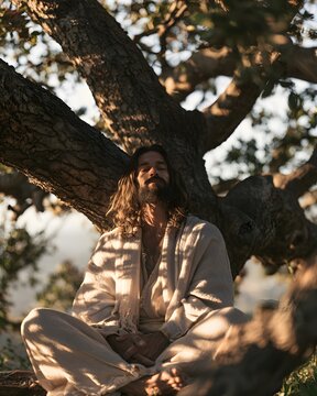 Peaceful bearded man meditating under a large tree in nature