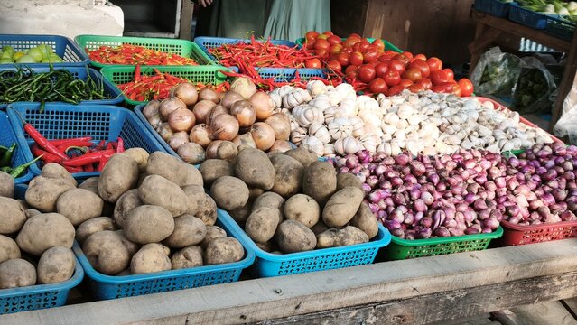 View of a vibrant market stall displaying baskets of fresh ginger, red chilies, garlic, limes, and onions