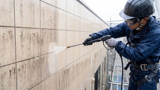 建物外壁のタイルに付着した黒ずみや汚れを足場上から高圧洗浄機で除去する、保護具を着用した作業員の外壁清掃作業