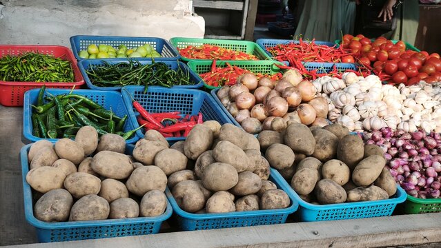 View of a vibrant market stall displaying baskets of fresh ginger, red chilies, garlic, limes, and onions