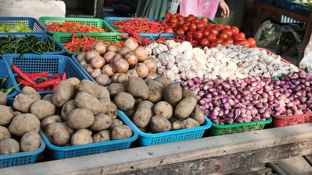 View of a vibrant market stall displaying baskets of fresh ginger, red chilies, garlic, limes, and onions