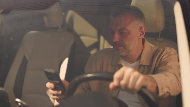 Mature man checking smartphone while sitting in car, depicting distracted driving, 4K