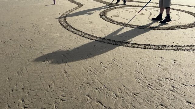 Shadows of volunteers creating a sand labyrinth on Face Rock Beach in Bandon, Oregon.