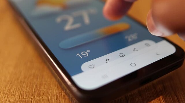 Human finger tapping a mobile phone screen, checking and sharing the temperature using a weather forecast app