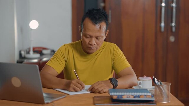 Student adult Asian man using laptop and writing on notebook. Learning, exam and education concept.