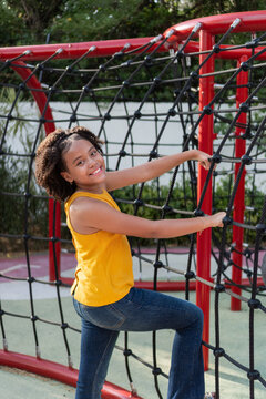 Happy teen girl climbing rope netting on playground