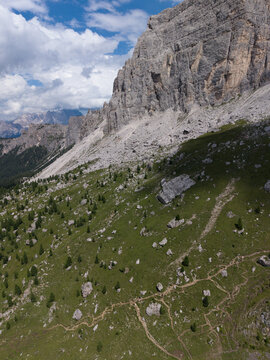 Aerial view of Monte Mondeval Corvo Alto, featuring rugged limestone cliffs, steep grassy slopes, boulders, and winding hiking trails in San Vito di Cadore, Veneto, Italy.