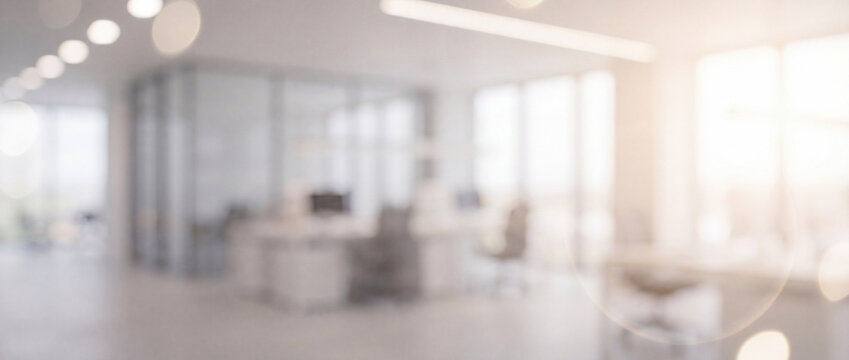 Blurred office interior background with soft light featuring bright neutral white tone, glass partitions, desks, and subtle bokeh flares, suitable for corporate banners and zoom backdrops