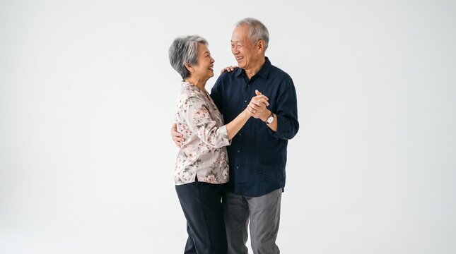 Happy senior couple dancing together in a bright studio while wearing casual clothing against a clean neutral white background backdrop
