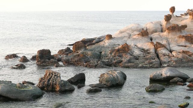 Sunken rocks on stony shore of cliff, Yehliu Geopark. Static camera, bright and crisp East China Sea waters and waves, wet rock in water, stones and bit of hoodoo mushroom stones field on right