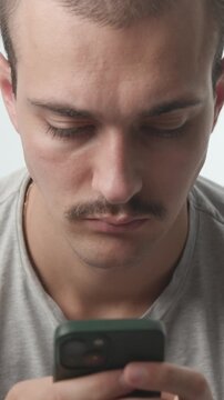 Close-up of a focused young man with a mustache typing on his smartphone, looking down at the screen against a bright studio background