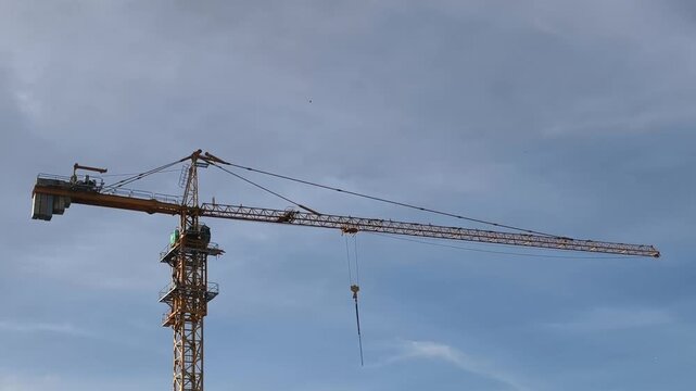 Tall yellow tower crane with lattice mast and extended jib set against a clear blue sky. The hook and cable system highlight construction engineering, making this image ideal for architecture theme. 