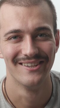 Close-up of a young man staring at the camera with a serious expression, then breaking into a genuine smile against a white background.