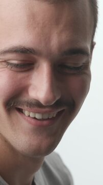 Close-up of a young man turning toward the camera with a big, cheerful smile and joyful laugh against a bright white background.