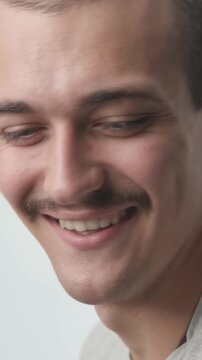 Close-up of a young man turning toward the camera with a big, cheerful smile and joyful laugh against a bright white background.