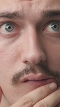Extreme close-up of a young man touching his chin with a pensive, thoughtful, and doubtful expression, looking up and away 