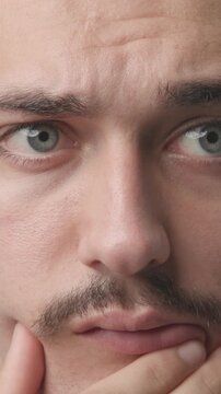 Extreme close-up of a young man touching his chin with a pensive, thoughtful, and doubtful expression, looking up and away 