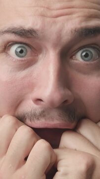 Extreme close-up of a young man with wide eyes looking scared, anxious, and terrified, biting his knuckles 