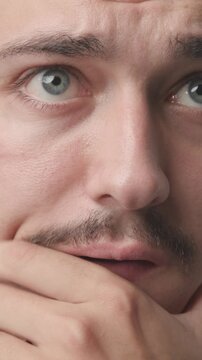 Extreme close-up of a young man looking shocked, anxious, and stressed, holding his face in his hands with a worried expression 