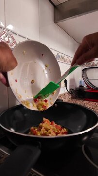 Slow motion footage showing a person pouring finely chopped vegetables into a hot pan with olive oil, preparing a classic soffritto base for a healthy vegetarian meal in a home kitchen