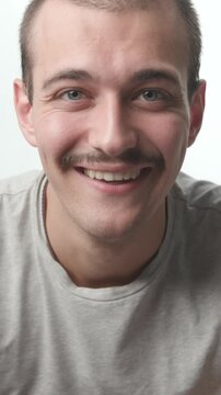 Close-up of a young man using a smartphone, looking up at the camera with a bright, friendly smile against a white background.