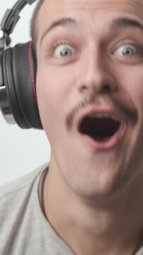 Close-up of a young man wearing headphones, looking shocked and amazed, then smiling and dancing with excitement against a white background.