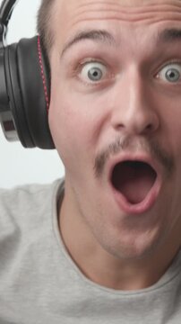 Close-up of a young man wearing headphones, looking shocked with open mouth, then raising his hands and cheering with excitement against a white background.