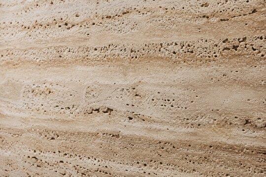 Travertine stone texture with natural horizontal striations and porous surface details in warm daylight