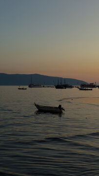 Small wooden fishing boat drifting in sea bay during calm pastel sunset in Vlore Albania