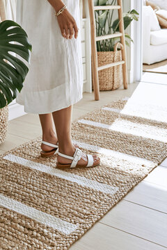 Woman's feet in white leather sandals stepping onto a woven jute runner in a modern coastal dressing room with natural light