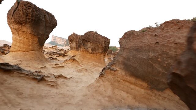 Unusual rock formations, mushroom stones at Yehliu Geopark. Glide shot, camera move across odd rocks over deserted field. Dusk evening time, soft natural light. Sponge hard cap on thin soft sandstone