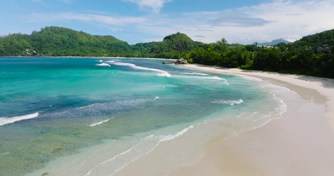 A pristine white sandy beach with turquoise waters stretching towards lush green hills and vegetation. Baie Lazare. Seychelles, Mahe.
