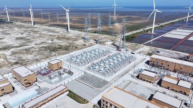 Aerial view of wind farm substation with transmission towers and wind turbines on coastal tidal flats