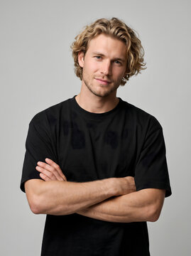 Young handsome man with curly blonde hair standing with arms crossed.