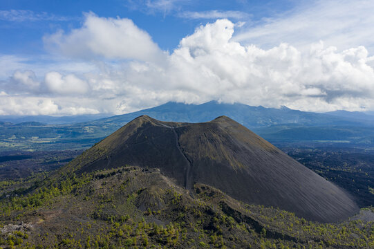 Aerial view of the cinder cone of Volcan Paricutin surrounded by volcanic landscape, sparse vegetation, and distant mountains under a blue sky in Uruapan, Michoacan, Mexico.