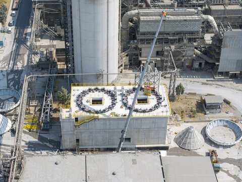 Aerial view of the TITAN Cement factory featuring industrial concrete structures, circular rooftop units, and a tall crane in Thessaloniki, Central Macedonia, Greece.
