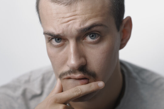 Thoughtful young man with mustache holding finger to lip in doubt