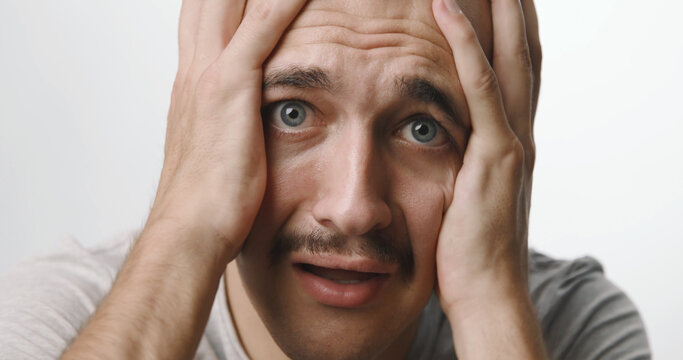 Portrait of a panicked young man holding his head in distress against a white studio background.