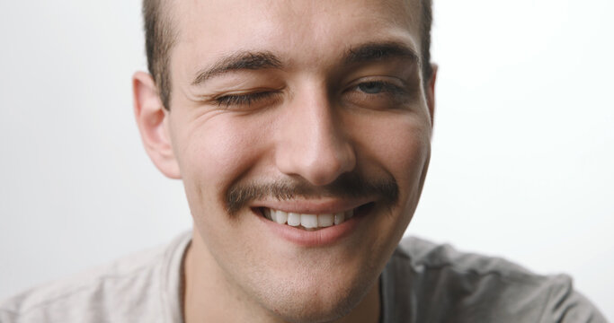 Portrait of happy young Caucasian man winking with mustache on white background.