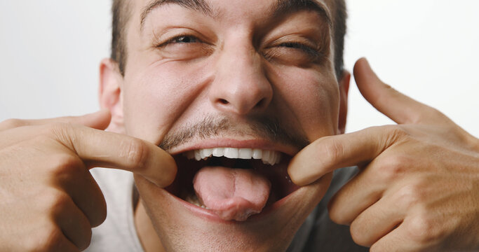 Funny young man with mustache pulling a silly face and sticking out his tongue against a white studio background.
