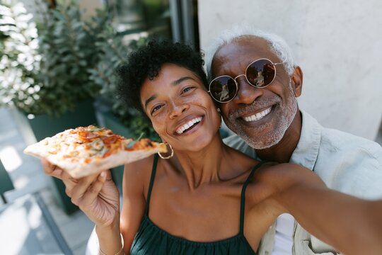 Joyful multigenerational duo enjoying pizza selfie together at a sunlit patio for lifestyle banner and background images