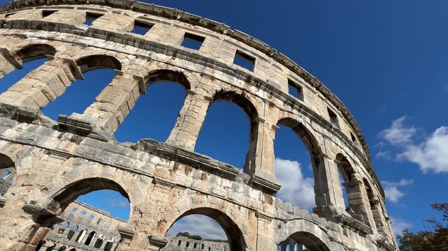 Ancient Roman amphitheater Pula, Croatia features arched openings and a weathered stone facade under a clear blue sky, highlighting its architectural beauty and historical context