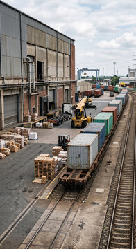 Elevated view of a rail freight terminal with parallel tracks, shipping containers and warehouse loading zones for intermodal cargo logistics