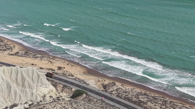 Drone view of the Makran Coastal Highway in Balochistan, Pakistan, featuring a scenic Arabian Sea coastline, rugged mountains, sandy beaches, winding road, and breathtaking coastal landscape.