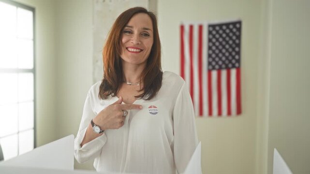 Woman points finger to i voted sticker at polling station inside voting booth with american flag visible; pride civic duty.