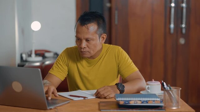 Student adult Asian man using laptop and writing on notebook. Learning, exam and education concept.