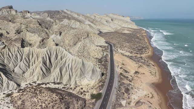 Aerial drone view of the Makran Coastal Highway in Balochistan, Pakistan, winding through rugged mountains along the Arabian Sea, showcasing dramatic coastline, scenic landscapes, and stunning natural