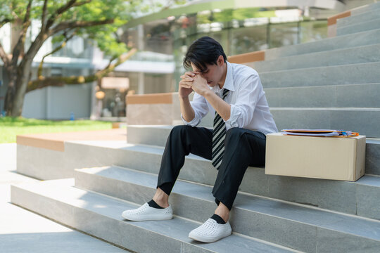 Unemployed man sitting on stairs holding resume feeling stressed and hopeless after getting fired.