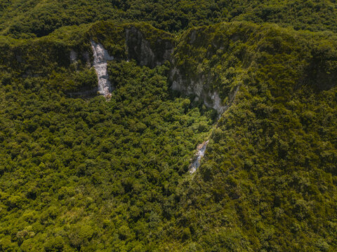 Aerial view of Laguna de Cuicocha featuring lush green volcanic crater slopes, dense forest vegetation, and rocky cliffs in Cotacachi, Imbabura, Ecuador.