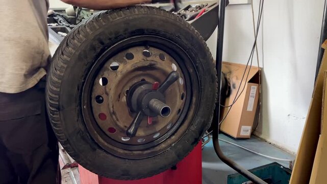 Close-up of a spinning car wheel mounted on a red balancing machine inside a garage. High-speed rotation during tire diagnostics or alignment process. Realistic auto service workshop environment.